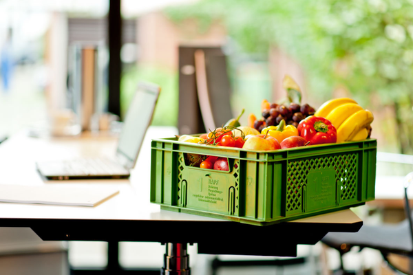 KI generiert: Ein Korb voller bunter Früchte und Gemüse steht auf einem Tisch neben einem Laptop.