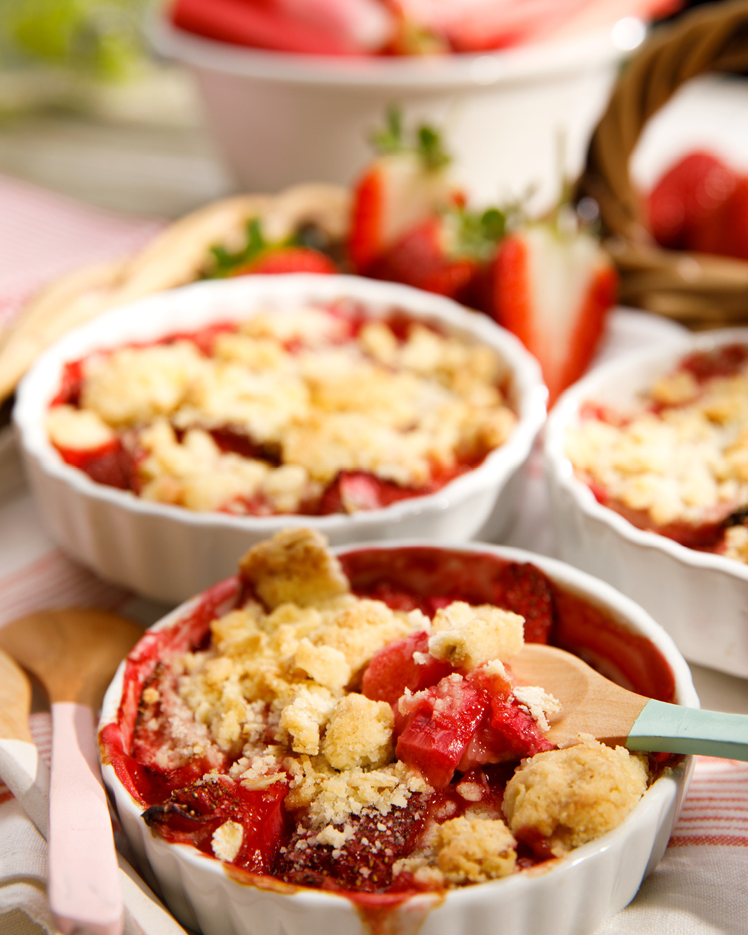 KI generiert: Kleine Auflaufformen mit Erdbeer-Crumble, dekoriert mit frischen Erdbeeren und Löffeln.