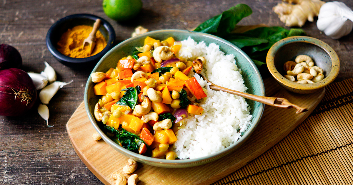ein Teller mit Reis und Gemüse-Curry, umgeben von Gewürzen und Nüssen.