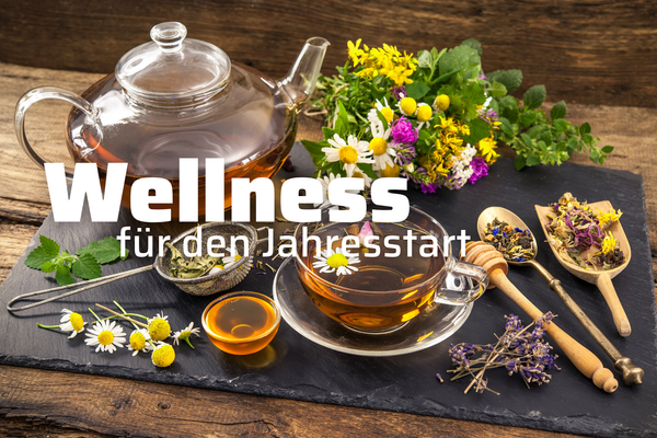 KI generiert: Das Bild zeigt eine Tee-Anordnung mit einer Glasteekanne, einer Tasse Tee und verschiedenen Kräutern und Blumen auf einem Schieferbrett. Der Text "Wellness für den Jahresstart" ist darauf platziert und betont einen entspannten, gesundheitsfördernden Beginn des Jahres.