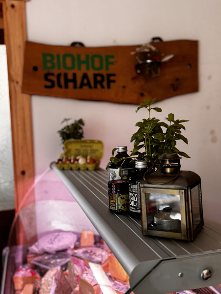 KI generiert: Regal mit Ölen, Kräutern und Eiern. Im Hintergrund ein Schild: "BIOHOF SCHARF".