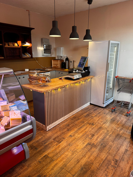 KI generiert: Ein kleiner Laden mit Tresen, Kühlschrank, Einkaufswagen und Käseauslage.