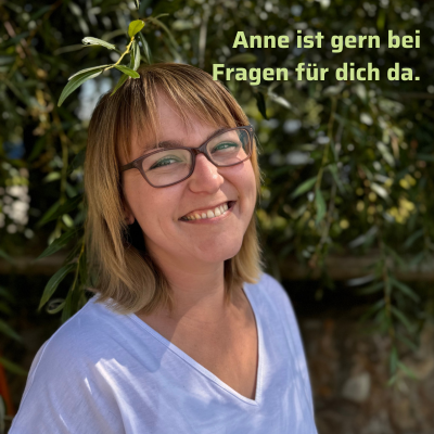 KI generiert: Eine Frau lächelt vor grünen Blättern. Text: „Anne ist gern bei Fragen für dich da.“