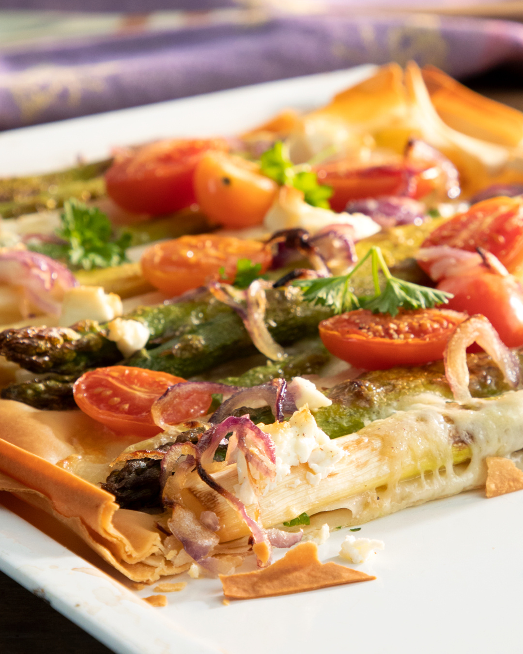 KI generiert: Ein Teller mit Spargel, Tomaten, Zwiebeln und Käse auf knusprigem Gebäck, garniert mit Kräutern.