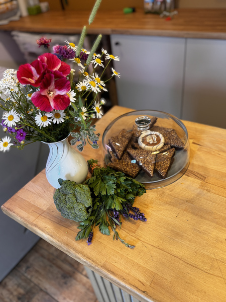 KI generiert: Ein Blumenstrauß und Gebäck auf einem Holztisch in einer Küche.
