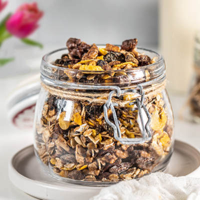 KI generiert: Ein Glas voller Müsli steht auf einem Teller, im Hintergrund eine Blume.