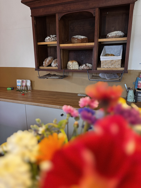 KI generiert: Holzregal mit verschiedenen Broten im Hintergrund, bunte Blumen unscharf im Vordergrund.